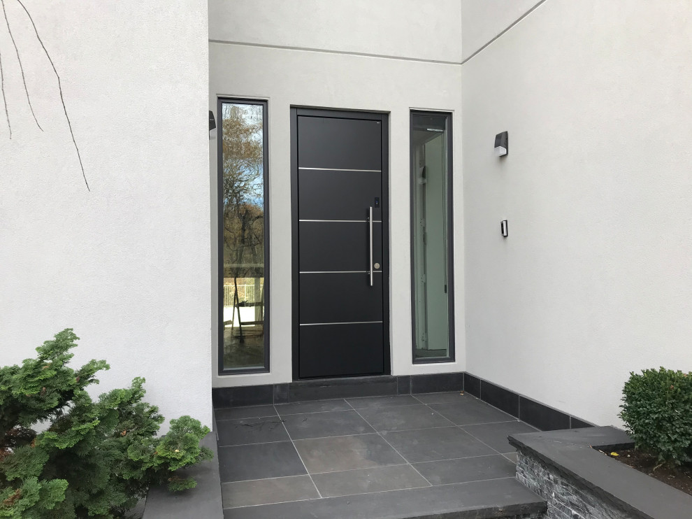 Aménagement d'une grande porte d'entrée moderne avec un mur gris, un sol en ardoise, une porte simple, une porte noire et un sol gris.