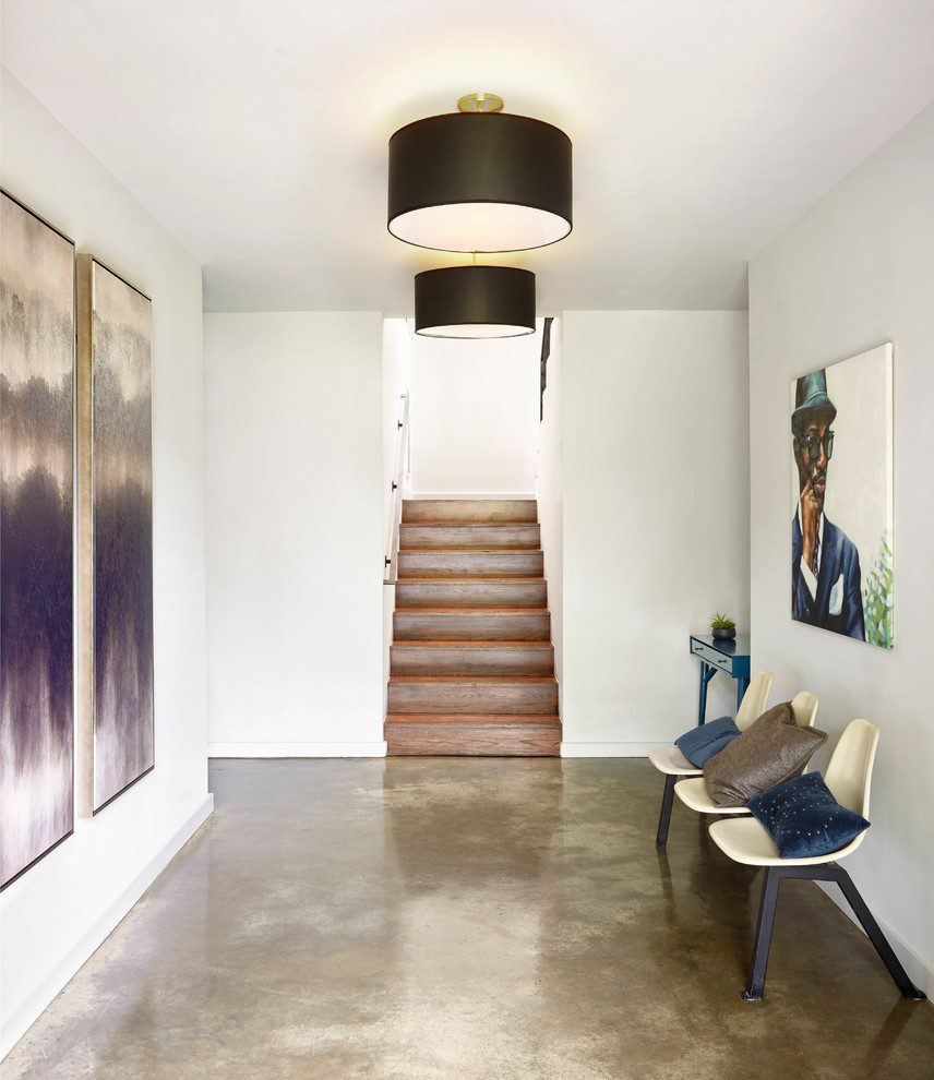 Cette image montre un grand hall d'entrée design avec un mur blanc, sol en béton ciré, une porte simple et un sol marron.