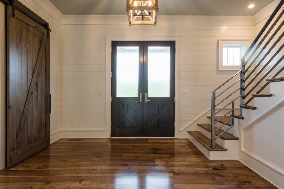 Réalisation d'une entrée champêtre de taille moyenne avec un couloir, un mur blanc, parquet foncé, une porte double, une porte en bois foncé et un sol marron.