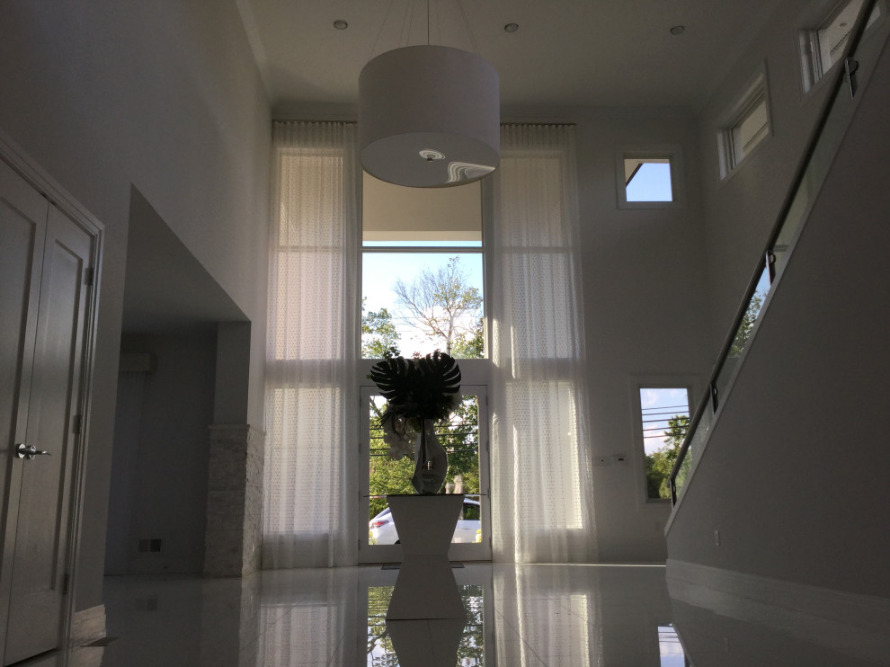 На фото: фойе среднего размера в стиле модернизм с белыми стенами, полом из керамогранита, двустворчатой входной дверью, стеклянной входной дверью и белым полом