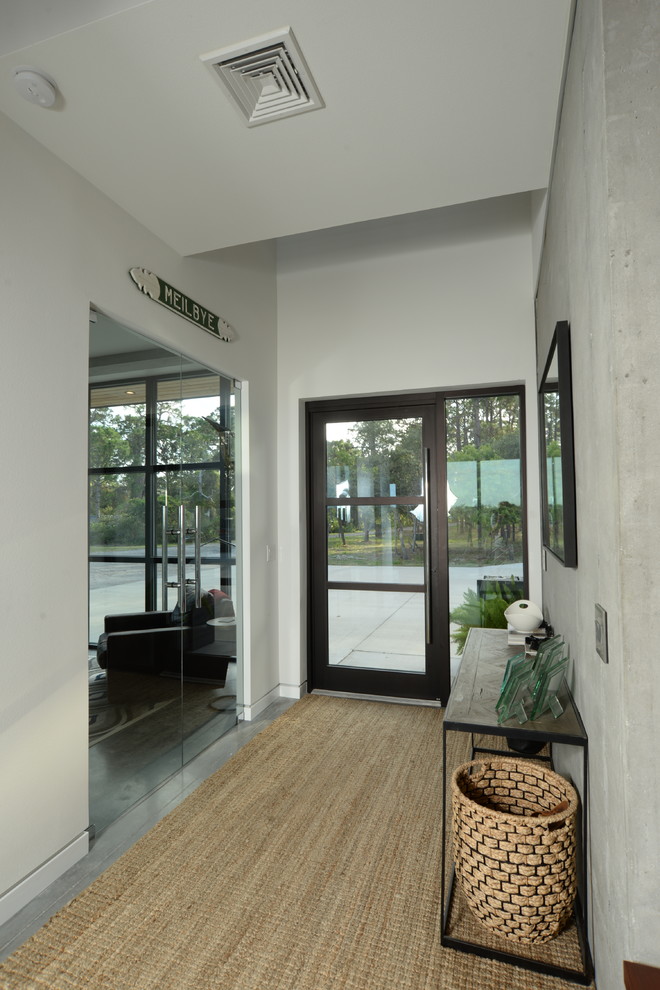 На фото: фойе среднего размера в стиле модернизм с белыми стенами, бетонным полом, поворотной входной дверью, стеклянной входной дверью и серым полом с