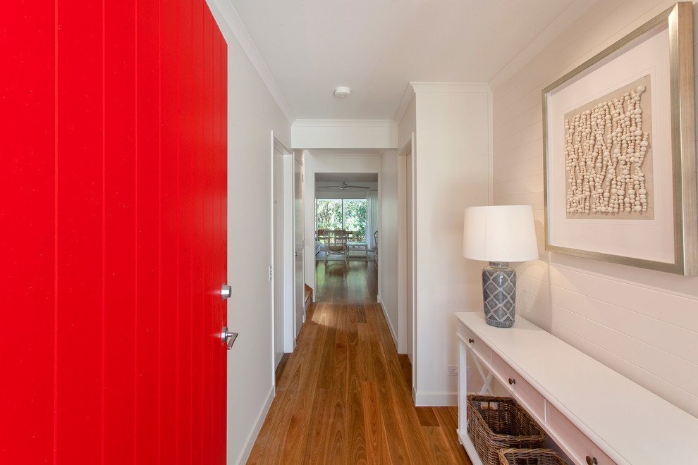 Modelo de hall costero de tamaño medio con paredes blancas, suelo de madera en tonos medios, puerta simple y puerta roja