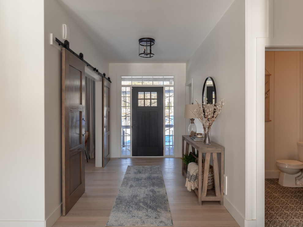Esempio di un grande corridoio chic con pareti bianche, parquet chiaro, una porta singola e una porta nera