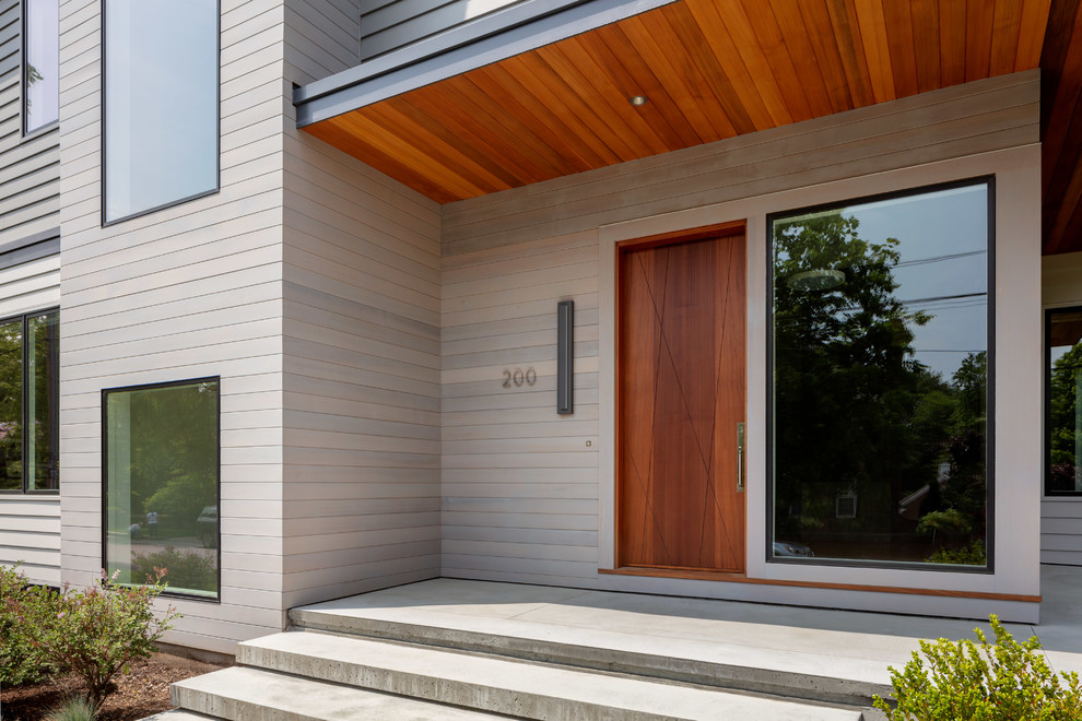Réalisation d'une grande porte d'entrée design avec sol en béton ciré, une porte simple, une porte en bois brun et un sol gris.