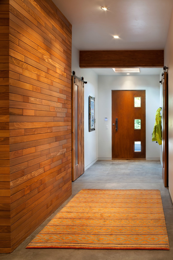 Cette image montre une grande entrée chalet avec sol en béton ciré, une porte métallisée, un couloir, un mur blanc et une porte simple.