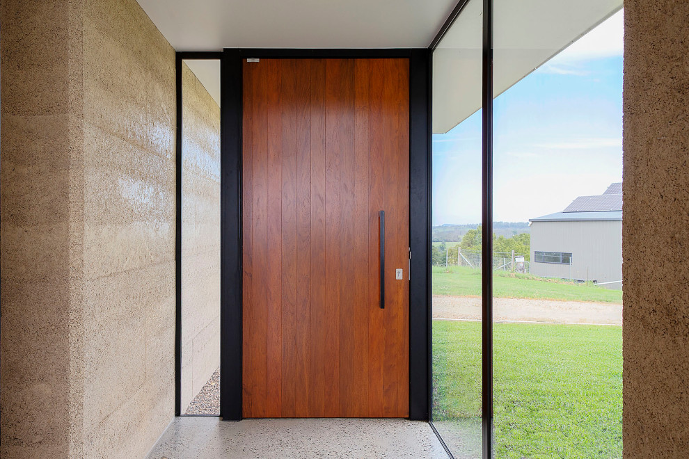 Diseño de puerta principal actual de tamaño medio con paredes beige, suelo de cemento, puerta pivotante, puerta de madera en tonos medios y suelo gris