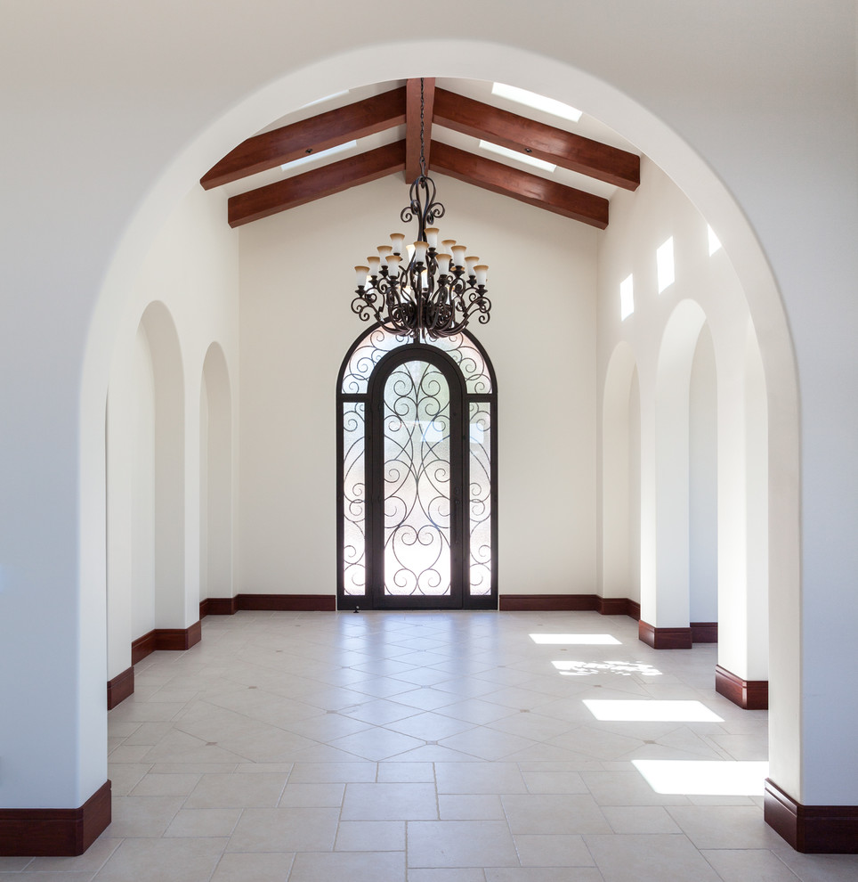 Cette image montre un grand hall d'entrée méditerranéen avec un mur blanc, un sol en carrelage de céramique, une porte simple et une porte en verre.