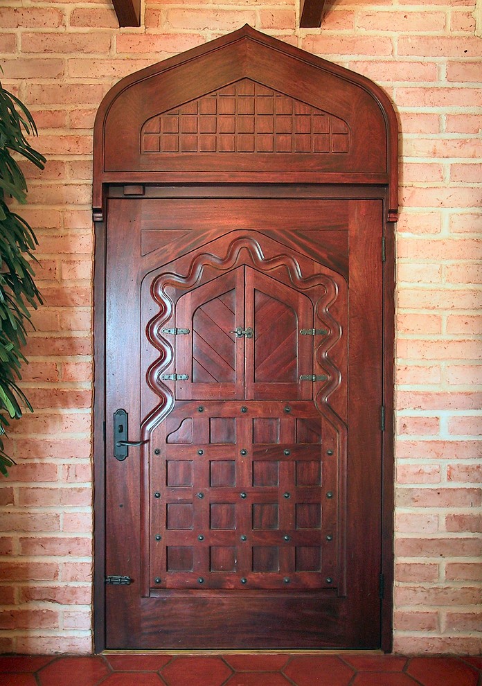 Cette image montre une grande porte d'entrée traditionnelle avec un mur orange, tomettes au sol, une porte simple et une porte en bois foncé.