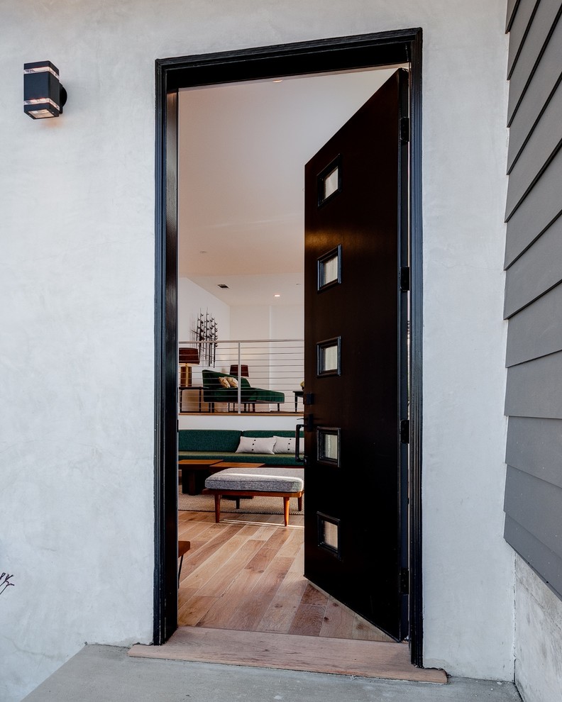 Réalisation d'une grande porte d'entrée design avec un mur blanc, parquet clair, une porte simple et une porte noire.