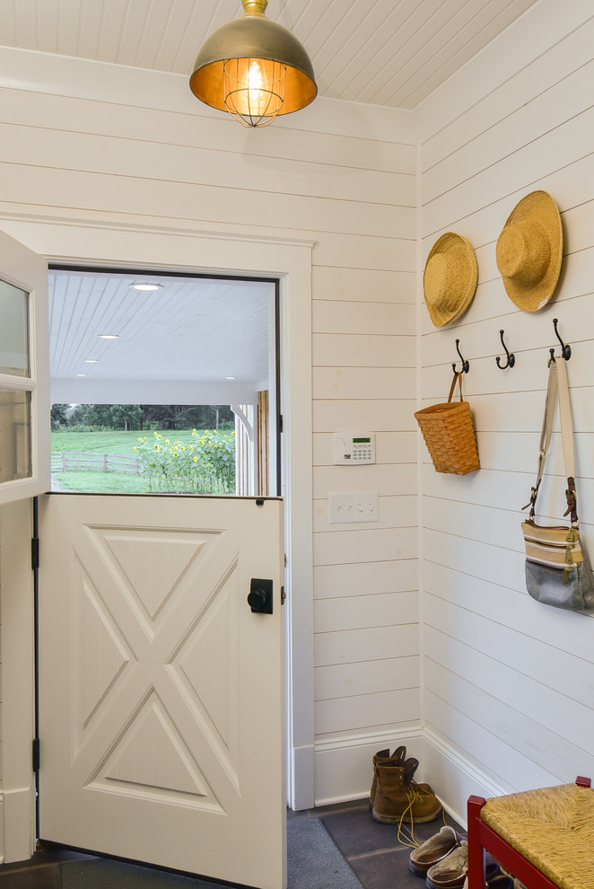 Modelo de vestíbulo posterior de estilo de casa de campo con paredes blancas, suelo de baldosas de porcelana, puerta tipo holandesa, puerta blanca y suelo negro