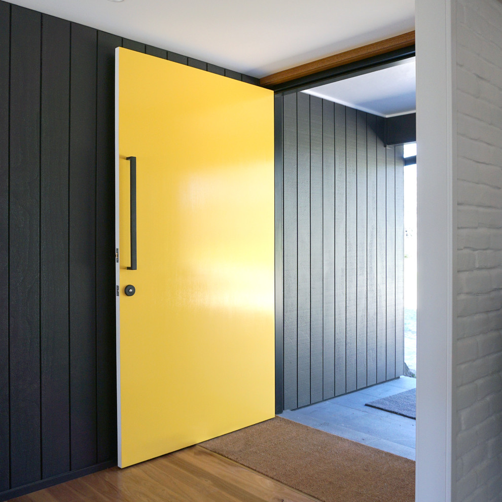 Aménagement d'une porte d'entrée contemporaine de taille moyenne avec un mur gris, un sol en bois brun, une porte simple et une porte jaune.