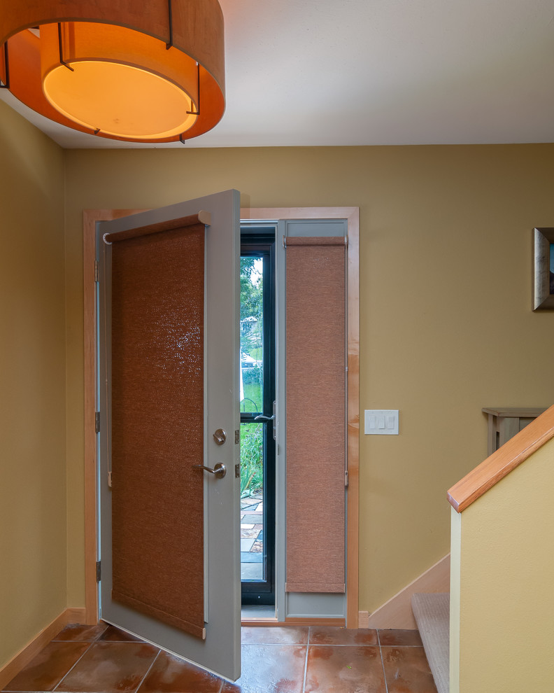 Cette photo montre une porte d'entrée tendance de taille moyenne avec un mur jaune, tomettes au sol, une porte simple et une porte blanche.
