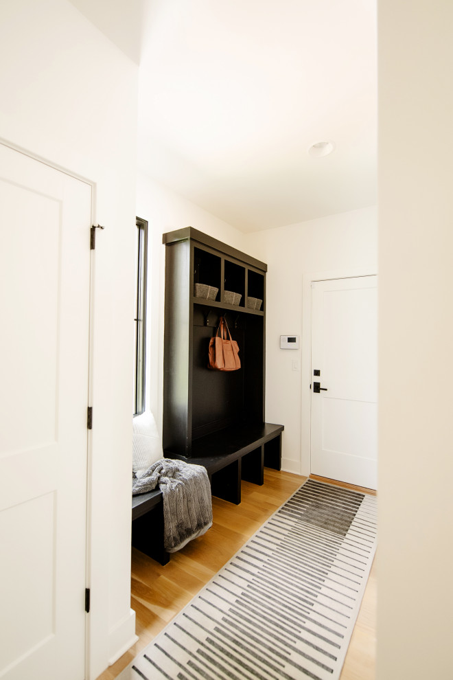 Cette photo montre une entrée tendance en bois avec un vestiaire, un mur blanc, parquet clair, une porte simple et une porte blanche.