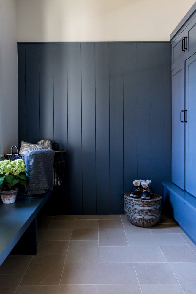 Réalisation d'une grande entrée chalet avec un vestiaire, un mur bleu, un sol beige et du lambris.