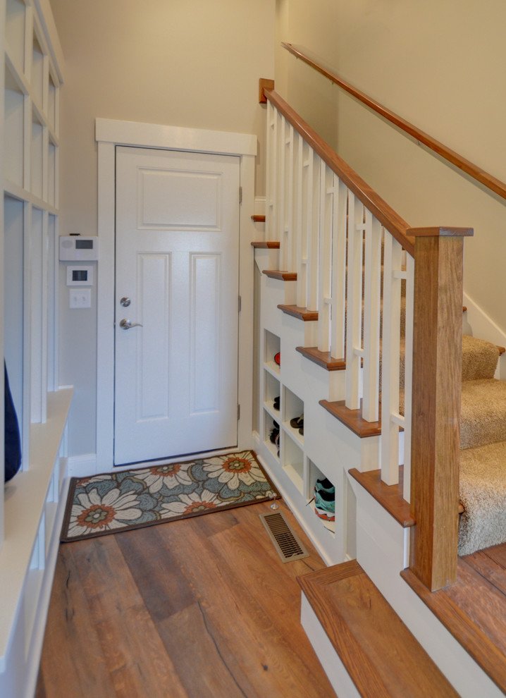 Aménagement d'une grande entrée craftsman avec un vestiaire, un mur beige, un sol en bois brun et une porte blanche.
