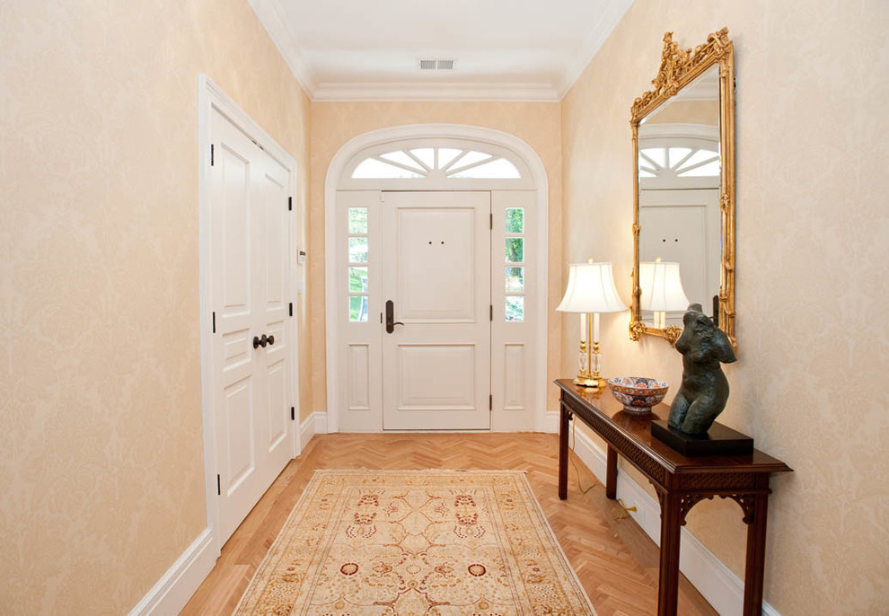 Exempel på en mellanstor klassisk foajé, med orange väggar, ljust trägolv, en vit dörr och en enkeldörr