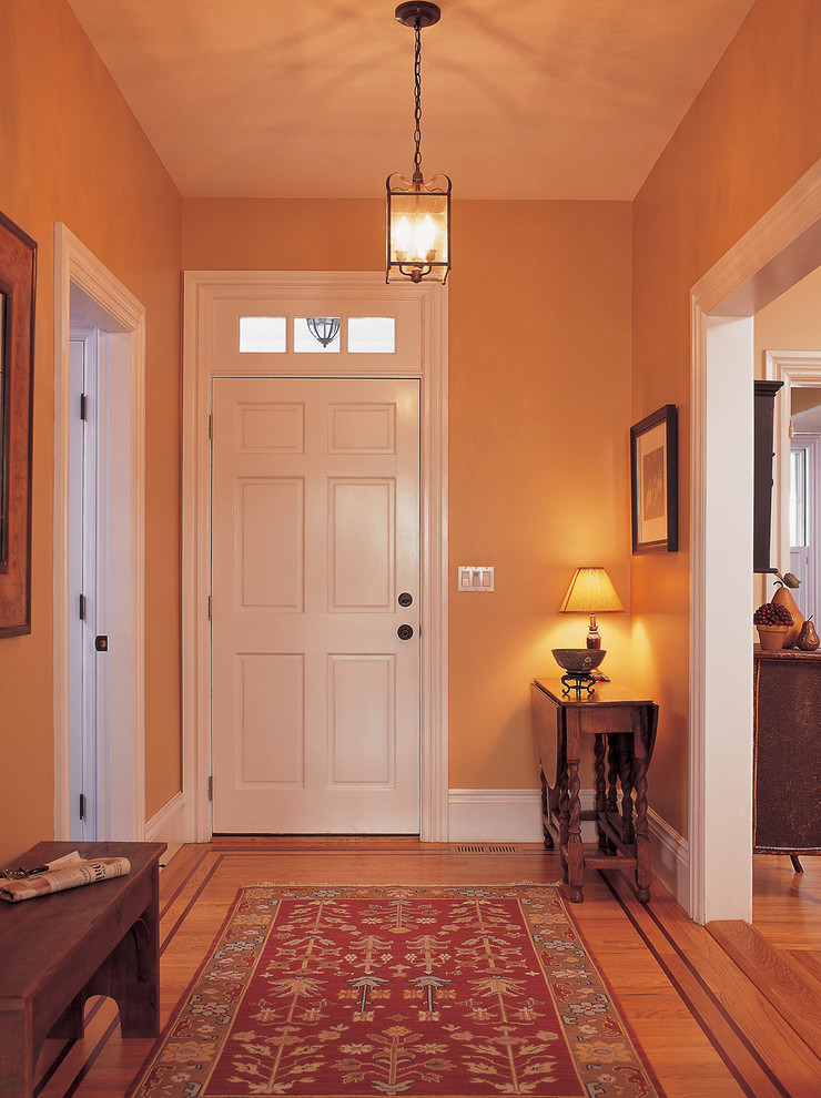 Cette image montre une entrée traditionnelle avec un couloir, un mur jaune, un sol en bois brun, une porte simple et une porte blanche.