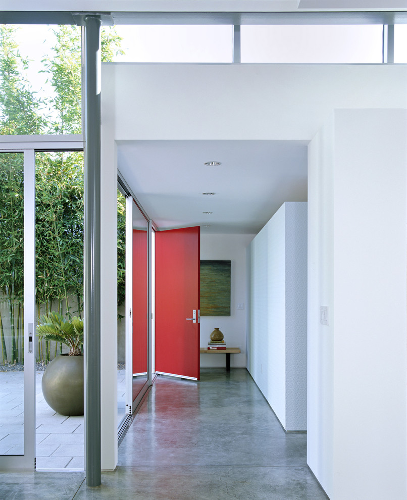 Bild på en mellanstor funkis foajé, med betonggolv, en röd dörr, grått golv, vita väggar och en enkeldörr