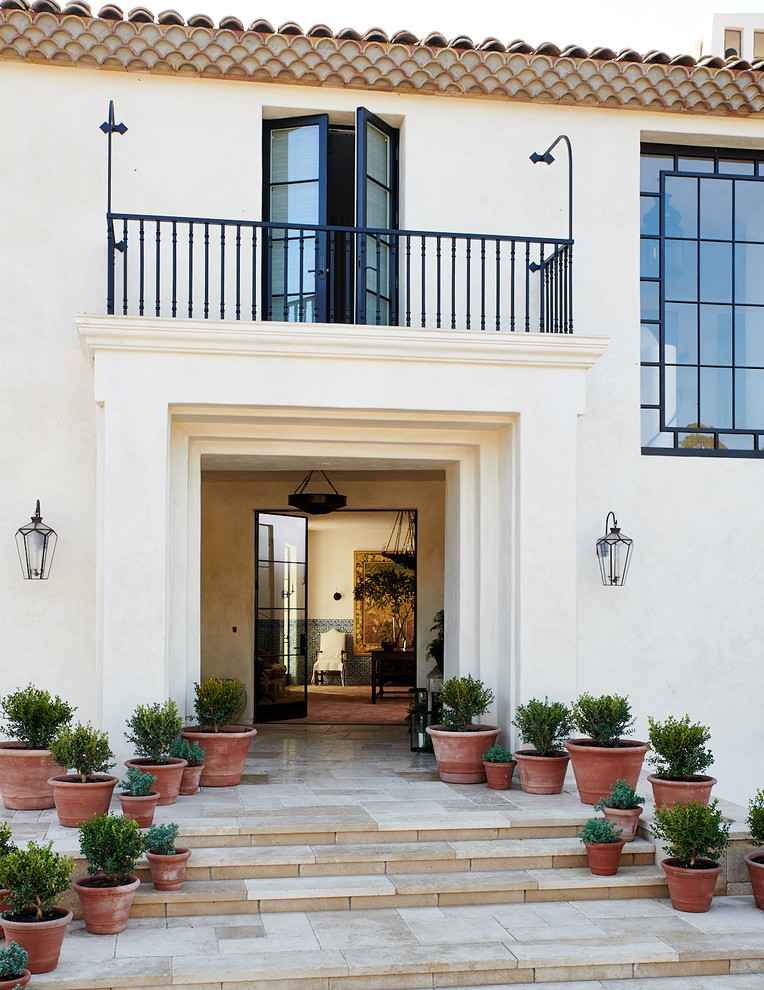 Inspiration for a mediterranean front door in Santa Barbara with white walls, a double front door, a glass front door, beige floors and feature lighting.