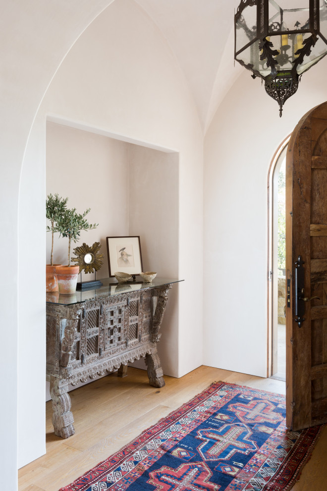 Ejemplo de distribuidor abovedado mediterráneo de tamaño medio con paredes beige, suelo de madera clara, puerta simple, puerta de madera en tonos medios y suelo beige