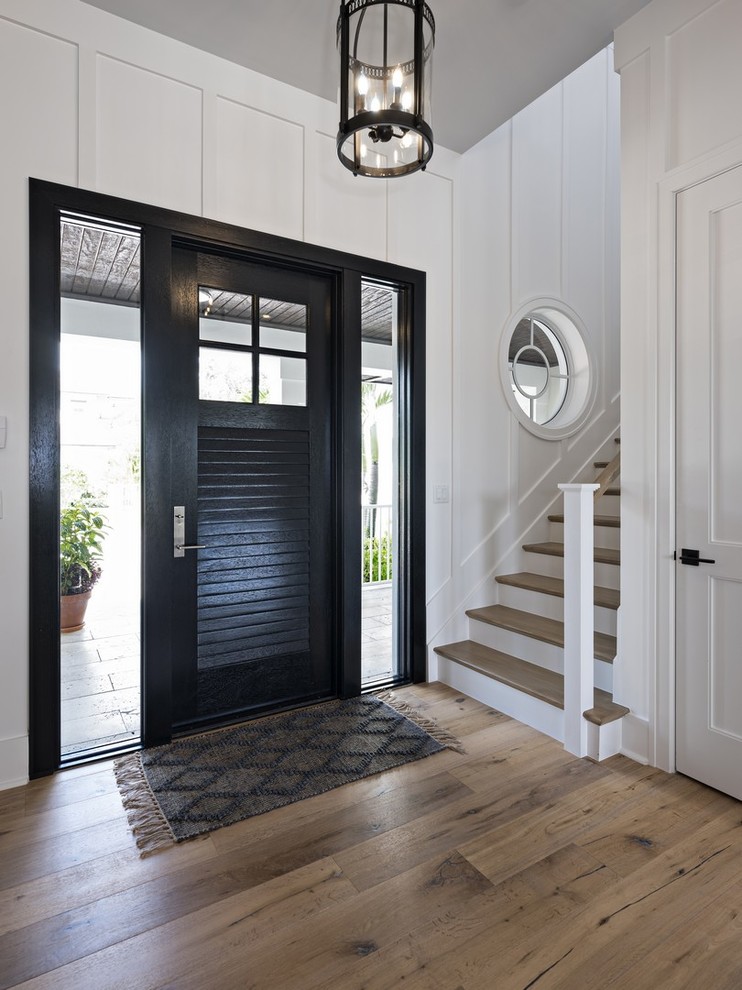 На фото: большое фойе в морском стиле с белыми стенами, паркетным полом среднего тона, одностворчатой входной дверью, черной входной дверью и коричневым полом