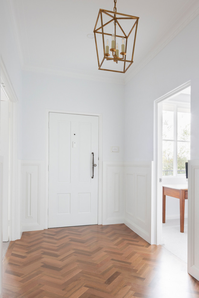 Exemple d'une entrée chic avec un sol en bois brun, une porte simple, une porte blanche et du lambris.