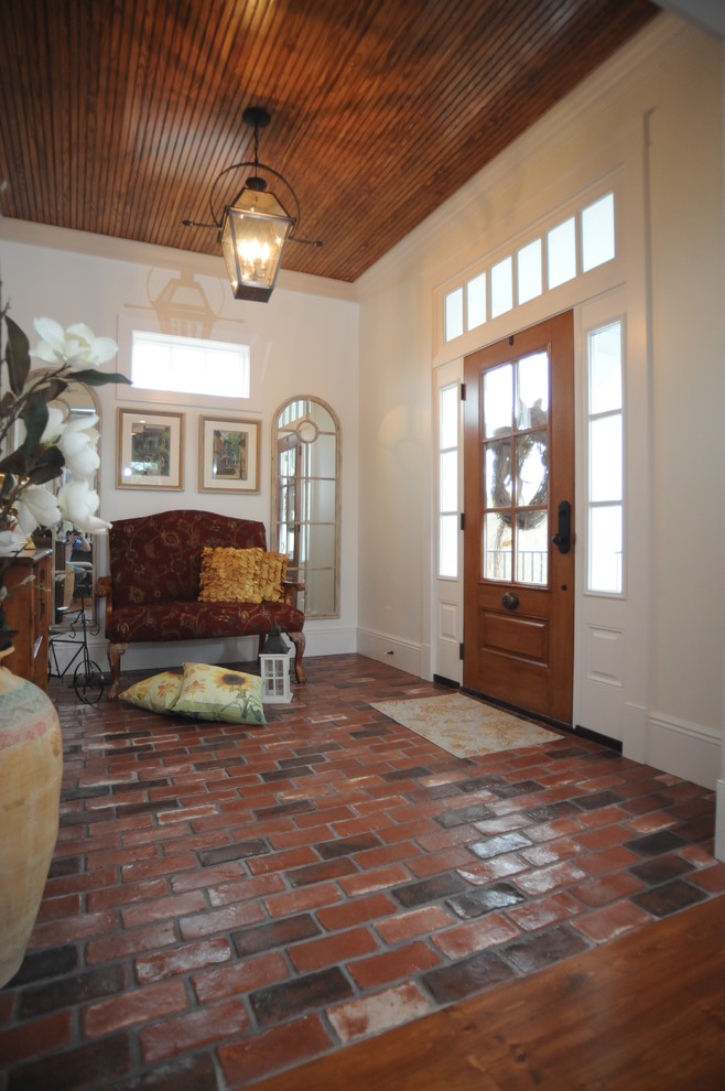 Пример оригинального дизайна: входная дверь среднего размера: освещение в стиле кантри с белыми стенами, кирпичным полом, одностворчатой входной дверью и входной дверью из светлого дерева