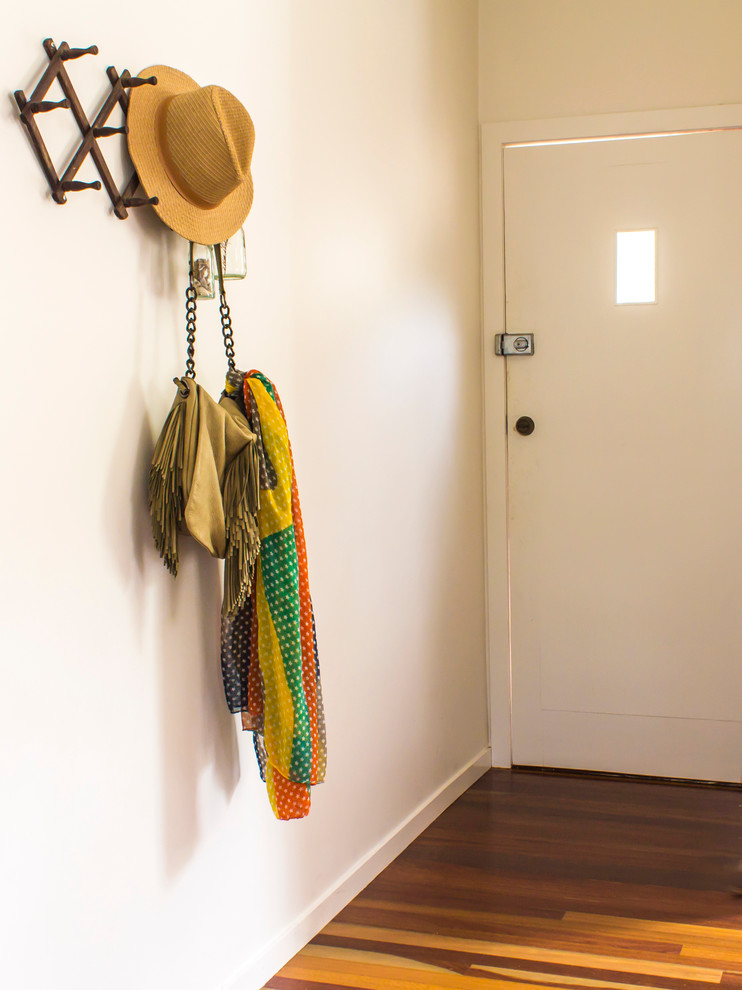This is an example of a small eclectic front door in Brisbane with white walls, medium hardwood flooring and a white front door.