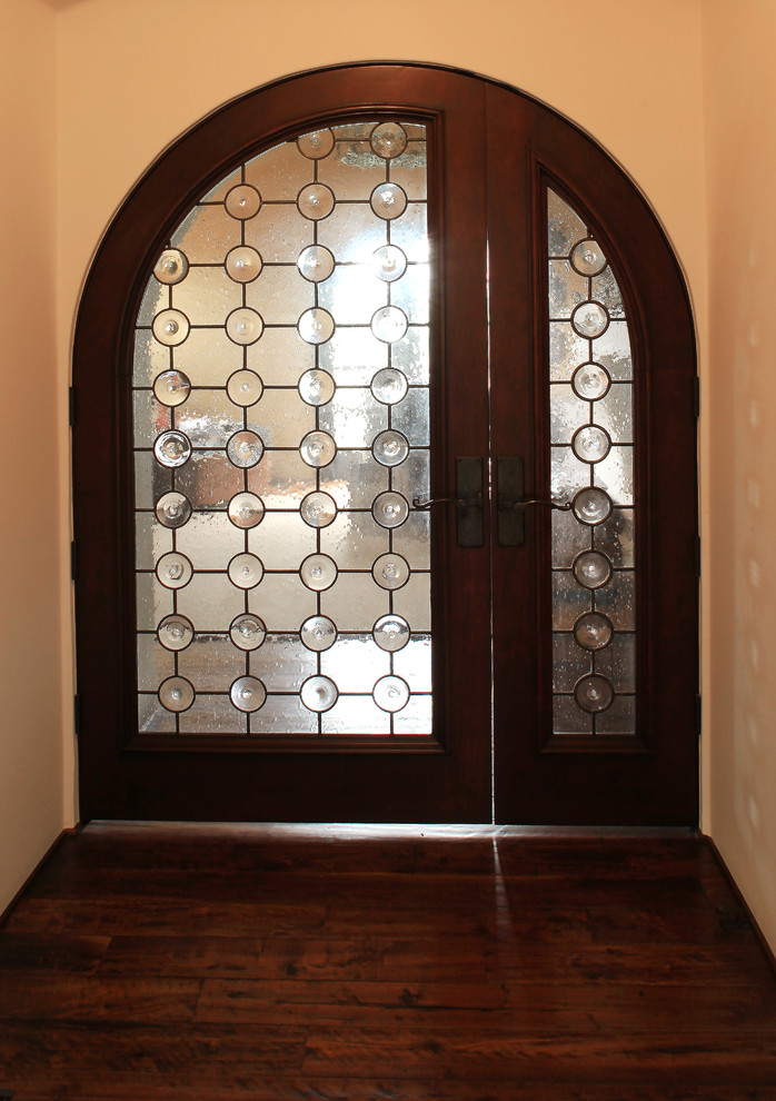 Diseño de puerta principal mediterránea con paredes blancas, suelo de madera oscura, puerta doble y puerta de vidrio