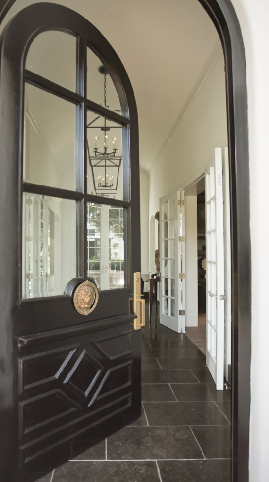 На фото: большая входная дверь с белыми стенами, полом из известняка, одностворчатой входной дверью, черной входной дверью и черным полом с