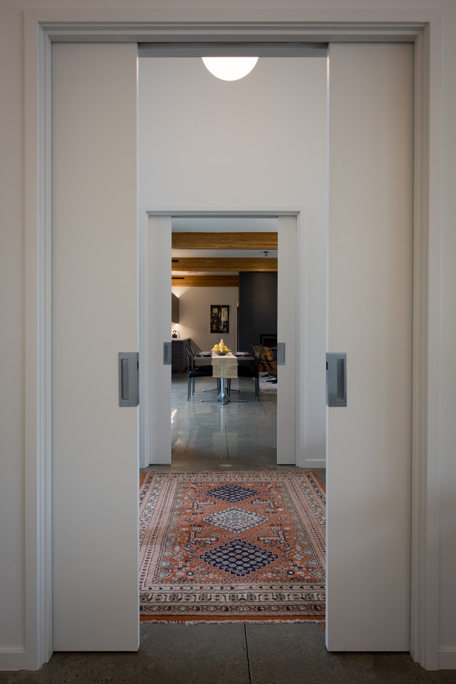 他の地域にある高級な中くらいなミッドセンチュリースタイルのおしゃれな玄関ロビー (白い壁、コンクリートの床、黒いドア、グレーの床) の写真