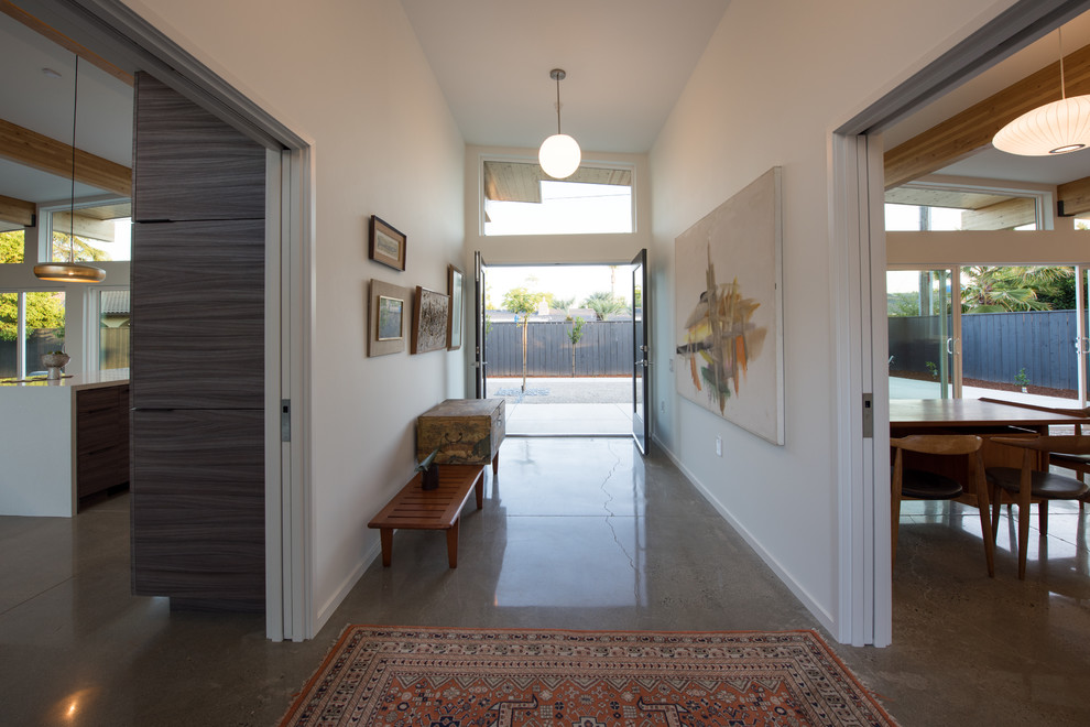 Cette photo montre un hall d'entrée rétro de taille moyenne avec un mur blanc, sol en béton ciré, une porte double, une porte noire et un sol gris.
