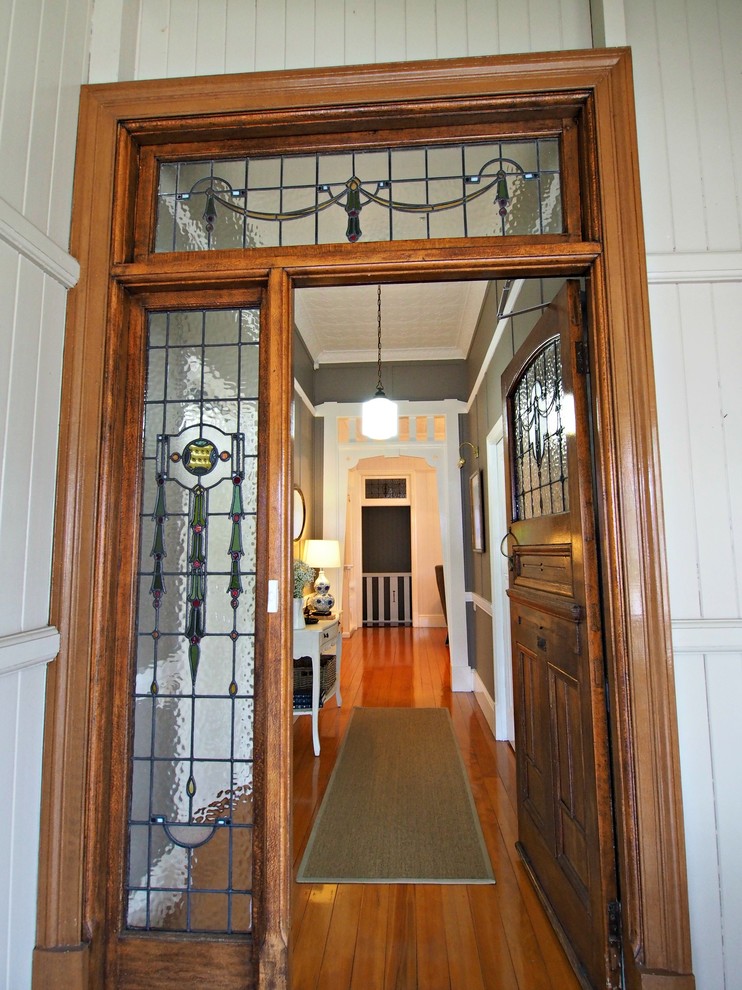 Exemple d'une grande entrée chic avec un mur gris, parquet clair, une porte pivot et une porte en bois brun.