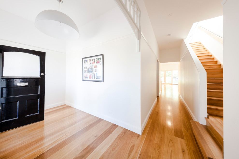 Modernes Foyer mit weißer Wandfarbe, braunem Holzboden, Einzeltür und schwarzer Haustür in Melbourne