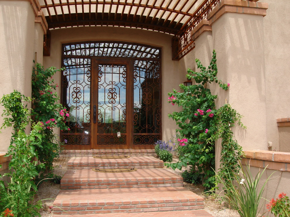 Aménagement d'une grande porte d'entrée sud-ouest américain avec un mur beige, un sol en brique, une porte simple, une porte métallisée et un sol rouge.