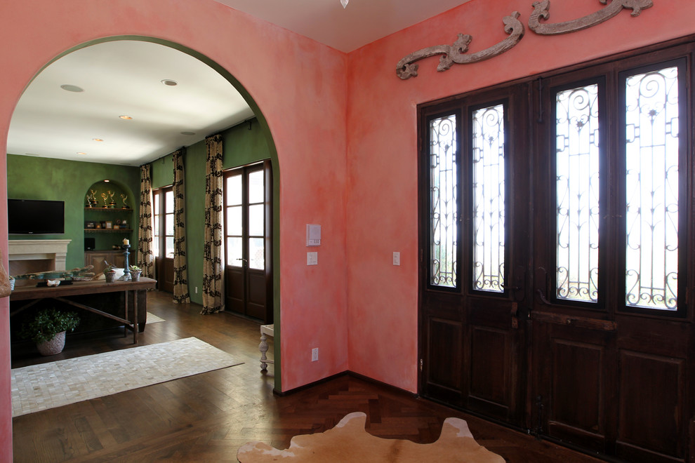 Пример оригинального дизайна: большое фойе в средиземноморском стиле с розовыми стенами, темным паркетным полом, двустворчатой входной дверью и коричневым полом