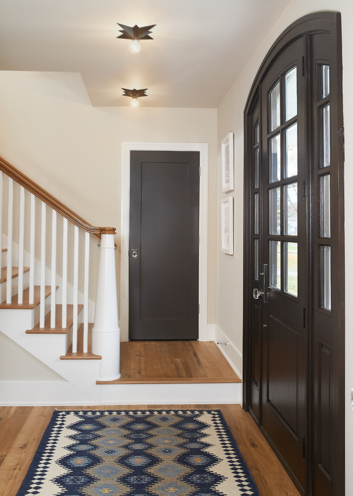 На фото: большое фойе в стиле неоклассика (современная классика) с одностворчатой входной дверью, белыми стенами, паркетным полом среднего тона, коричневой входной дверью и коричневым полом