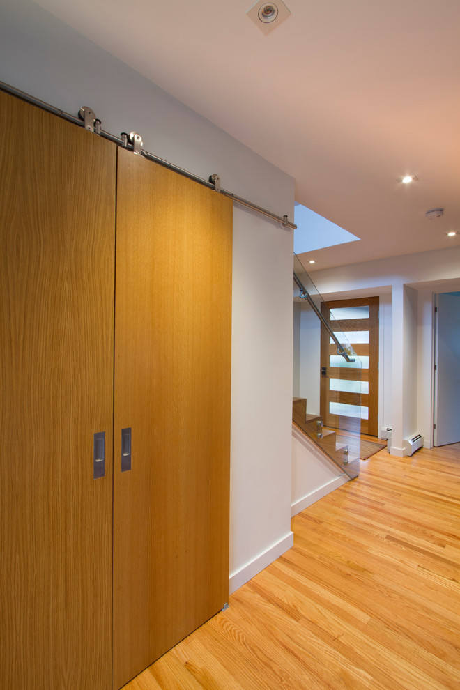 Esempio di un corridoio design di medie dimensioni con pareti bianche, pavimento in legno massello medio, una porta singola, una porta in legno chiaro e pavimento marrone