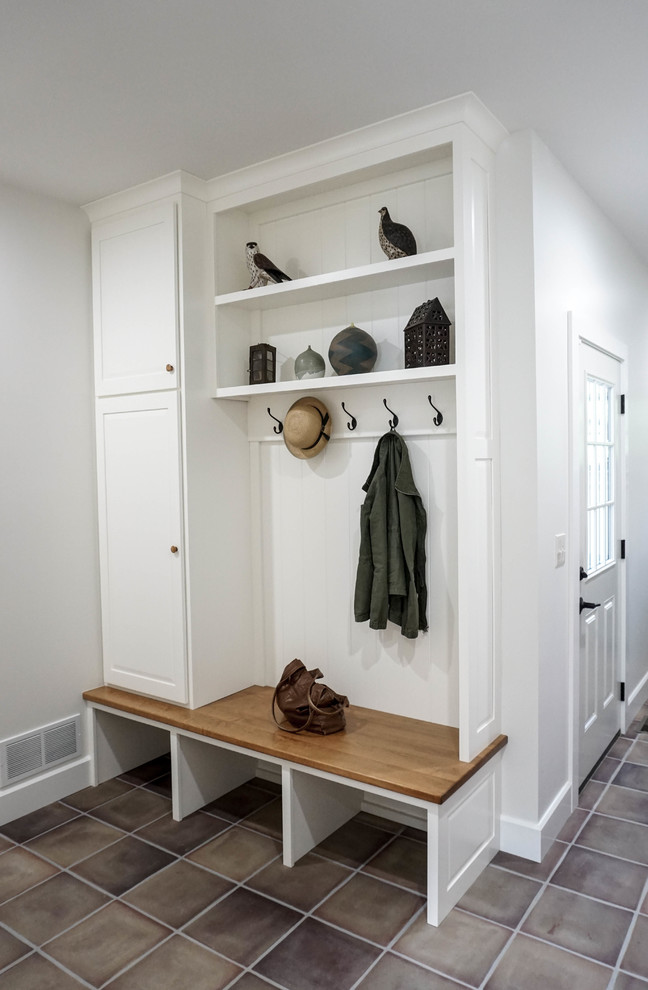 Example of a mid-sized farmhouse ceramic tile and brown floor mudroom design in Other with white walls