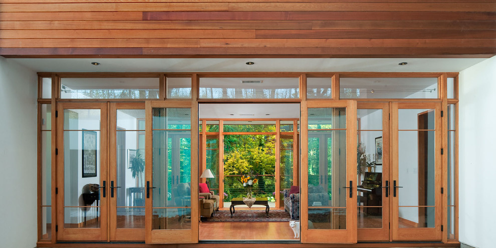 Cette photo montre un grand hall d'entrée tendance avec un mur blanc, un sol en bois brun, une porte double et une porte en verre.