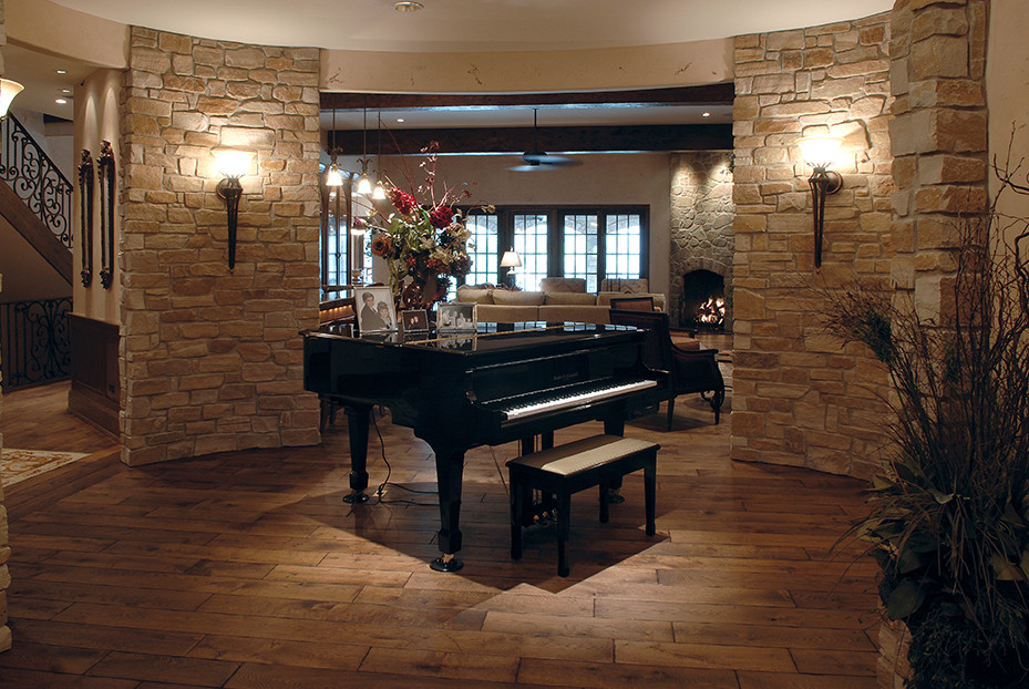Cette photo montre un très grand salon chic avec un bar de salon, un sol en bois brun, une cheminée standard, un manteau de cheminée en pierre, un sol marron et poutres apparentes.