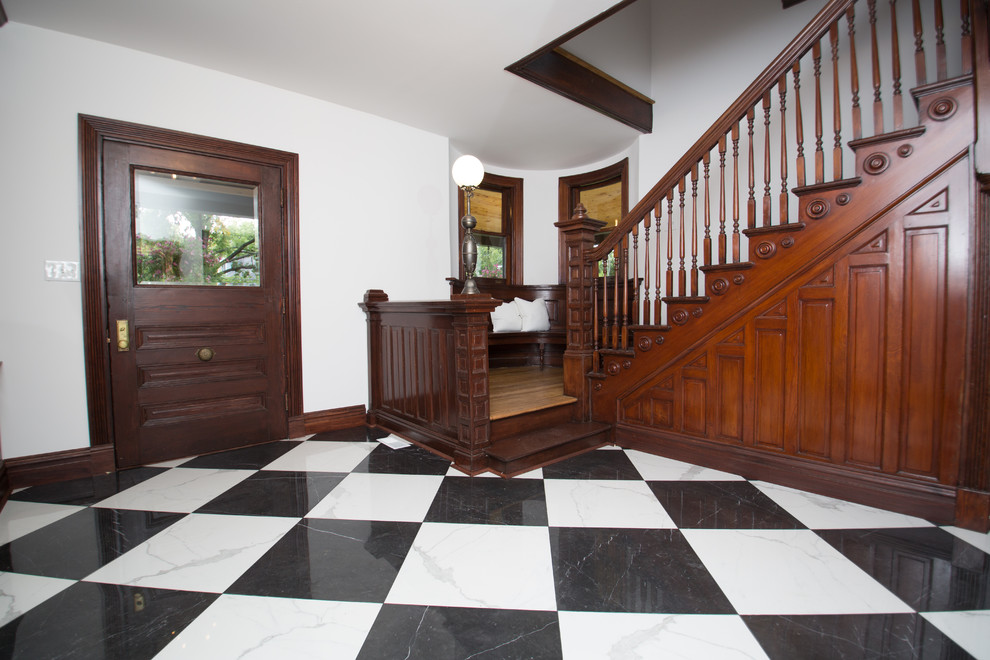 セントルイスにあるヴィクトリアン調のおしゃれな玄関ロビー (白い壁、磁器タイルの床、濃色木目調のドア) の写真