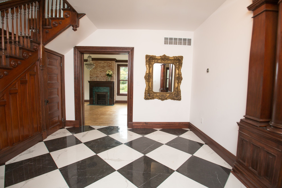 セントルイスにあるヴィクトリアン調のおしゃれな玄関ロビー (白い壁、磁器タイルの床、濃色木目調のドア) の写真