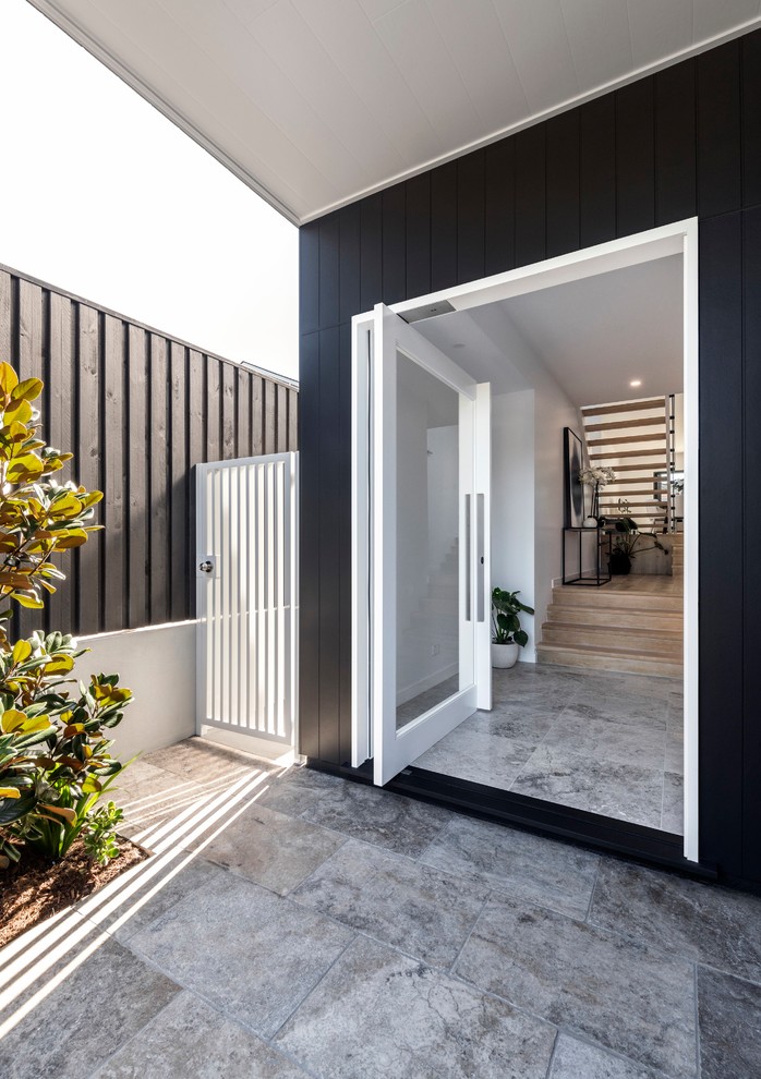 Foto di un grande ingresso moderno con pareti nere, pavimento in travertino, una porta a pivot, una porta in vetro e pavimento grigio