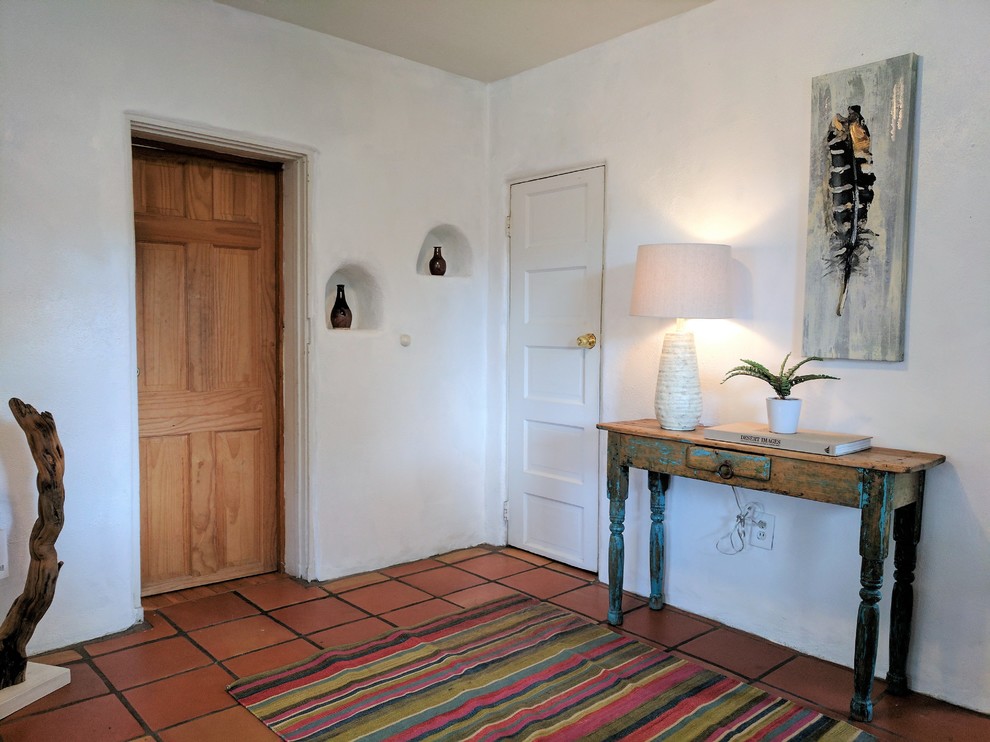 Inredning av en amerikansk liten foajé, med vita väggar, klinkergolv i terrakotta, en enkeldörr, en brun dörr och orange golv