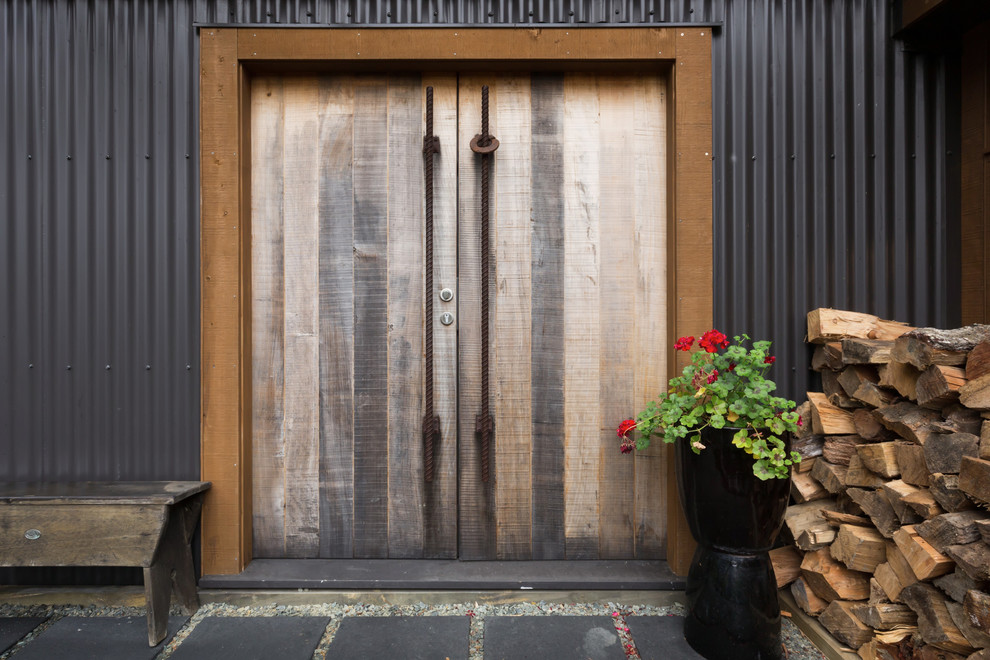 オークランドにあるインダストリアルスタイルのおしゃれな玄関 (黒い壁、スレートの床、木目調のドア) の写真