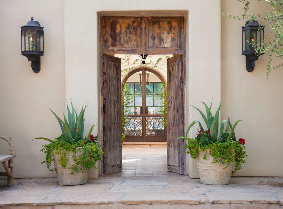 Cette image montre une porte d'entrée méditerranéenne avec une porte double et une porte en bois brun.