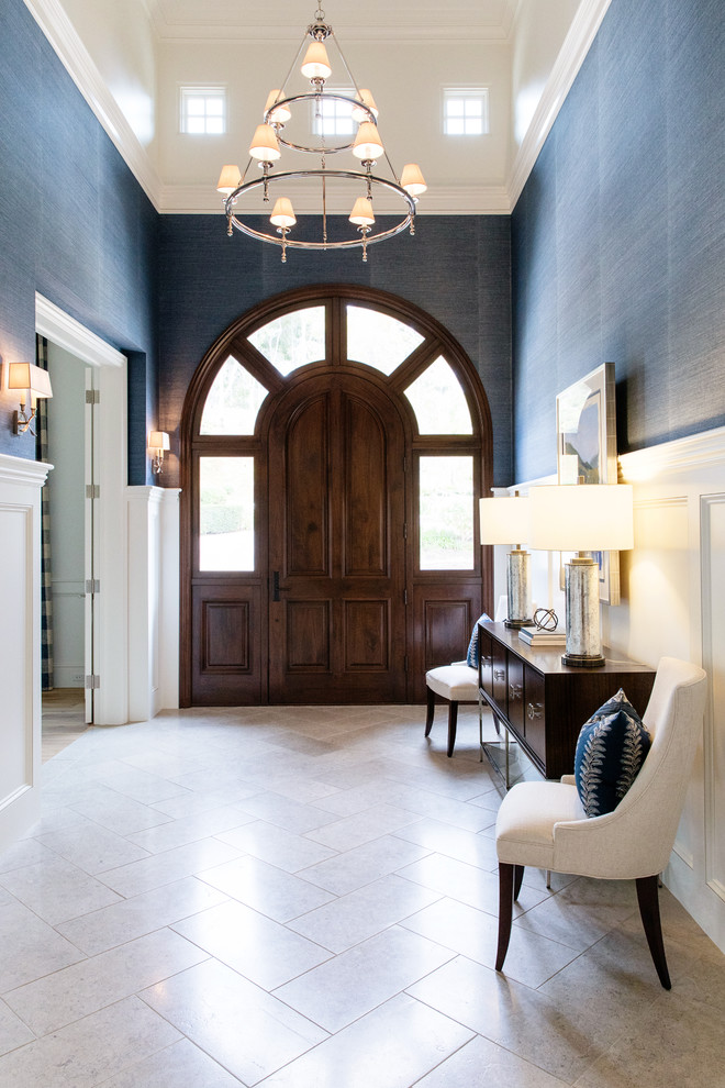 На фото: большое фойе в стиле неоклассика (современная классика) с синими стенами, полом из известняка, одностворчатой входной дверью, коричневой входной дверью и бежевым полом