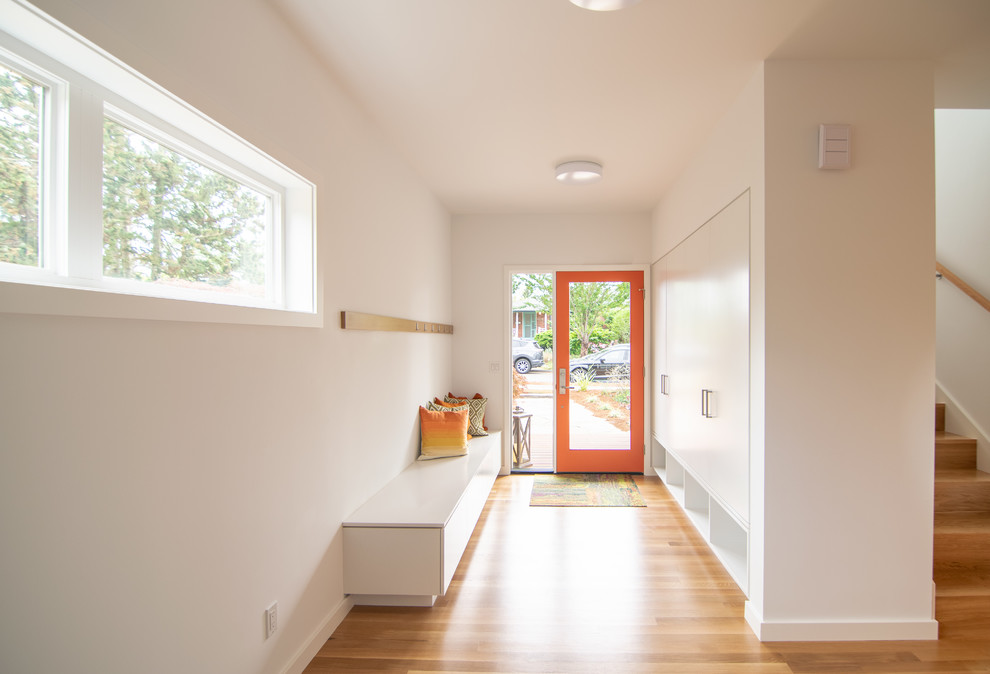 Modelo de distribuidor minimalista de tamaño medio con paredes blancas, suelo de madera en tonos medios, puerta simple, puerta naranja y suelo marrón