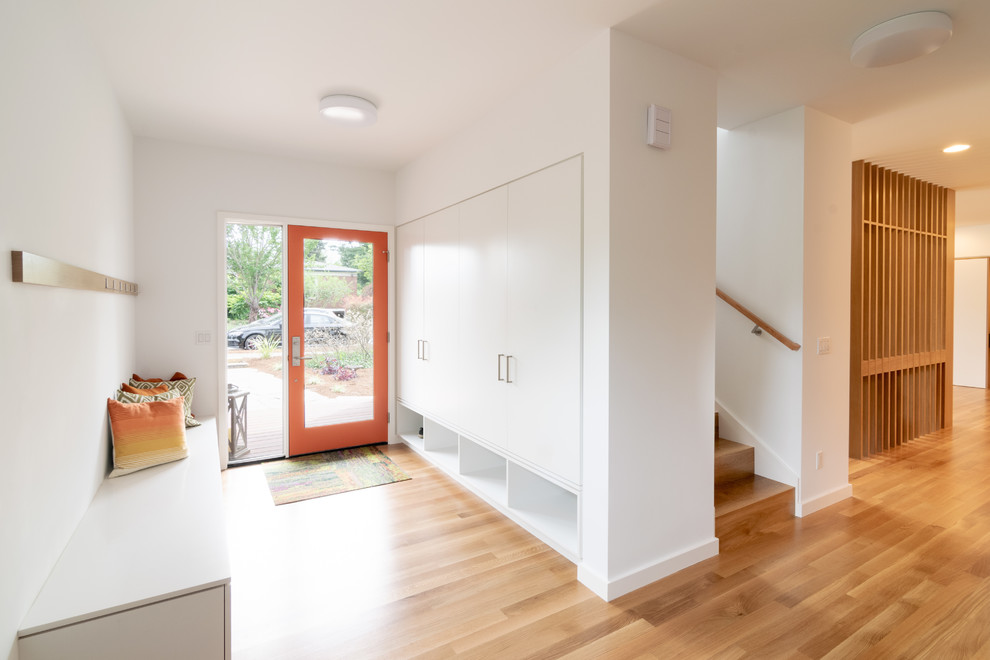 Ispirazione per un ingresso moderno di medie dimensioni con pareti bianche, pavimento in legno massello medio, una porta singola, una porta arancione e pavimento marrone